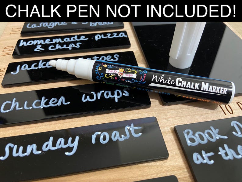 May include: A black chalkboard with a white chalk marker. The chalkboard is divided into seven sections, each labeled with a day of the week. The sections are filled with handwritten text, such as "lasagne", "homemade pizza", "chicken wraps", and "Sunday roast". The text "CHALK PEN NOT INCLUDED!" is printed at the top of the chalkboard.