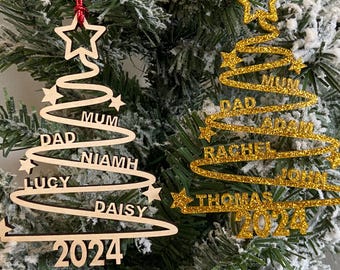 May include: Two wooden Christmas tree ornaments with names and the year 2024. The ornament on the left is natural wood with the names Lucy, Daisy, Niamh, Dad, Mum. The ornament on the right is gold glitter with the names Thomas, John, Rachel, Adam, Dad, Mum.