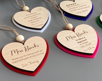 May include: Heart-shaped wooden ornaments with personalized messages for teachers. Each ornament has a wooden top layer and a colored acrylic base in red, pink, blue, and green. The ornaments are strung with twine and a wooden bead.
