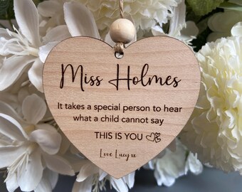 May include: A wooden heart-shaped ornament with the inscription "Miss Holmes." The text below reads "It takes a special person to hear what a child cannot say. THIS IS YOU." A small wooden bead is at the top for hanging. The background is white flowers.