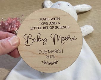 May include: A round wooden sign with the text "Made with love and a little bit of science Baby Moore Due March 2025" and a small floral design.