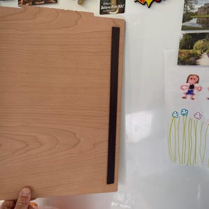 May include: A light wood magnetic dry erase board with black magnetic strips on the sides. The board is hanging on a white surface.