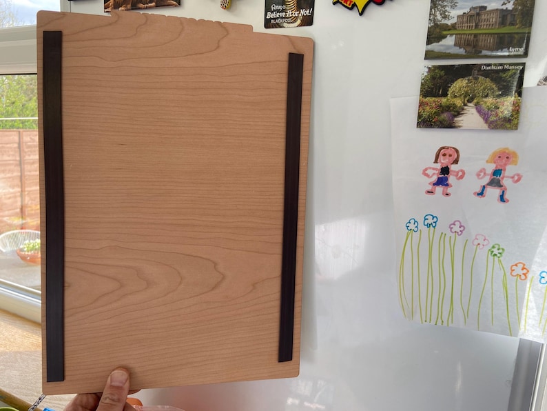May include: A light wood magnetic dry erase board with black magnetic strips on the sides. The board is hanging on a white surface.