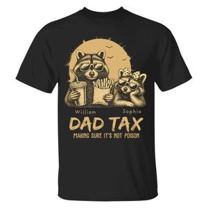 May include: Black t-shirt with a graphic of two raccoons in sunglasses, one with a drink and the other with fries, and the text "DAD TAX MAKING SURE IT'S NOT POISON". The design includes a sun and birds.