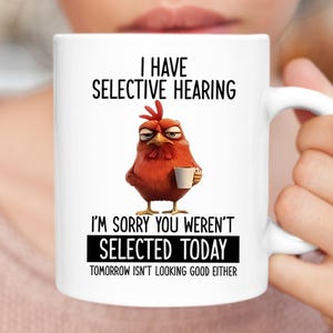 Peut inclure: Mug en céramique blanche avec un dessin de poulet en colère tenant une tasse à café. Le texte sur la tasse dit : "I HAVE SELECTIVE HEARING" et "I'M SORRY YOU WEREN'T SELECTED TODAY".