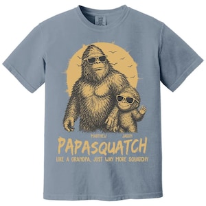May include: A blue t-shirt with a graphic of a Bigfoot wearing sunglasses and a smaller Bigfoot. The text says "Papasquatch" and "Like a grandpa, just way more squatchy."