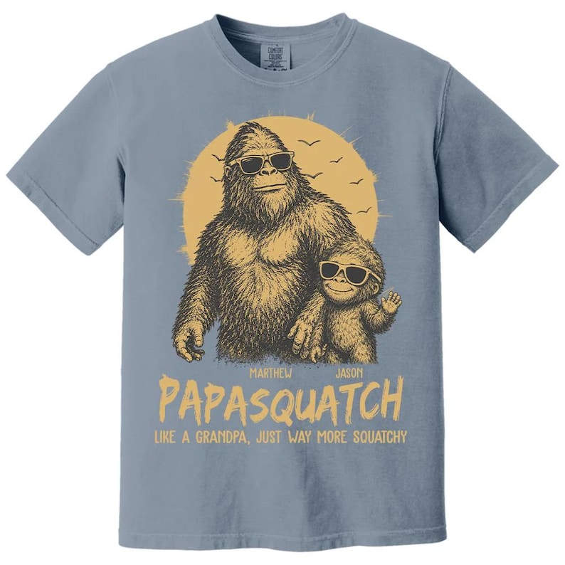 May include: A blue t-shirt with a graphic of a Bigfoot wearing sunglasses and a smaller Bigfoot. The text says "Papasquatch" and "Like a grandpa, just way more squatchy."