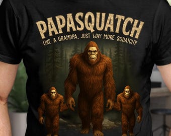 May include: Black t-shirt featuring a graphic of a Bigfoot family with the text "PAPASQUATCH LIKE A GRANDPA, JUST WAY MORE SQUATCHY". The Bigfoot family includes Sarah, David, and John. The design is in shades of brown and tan.