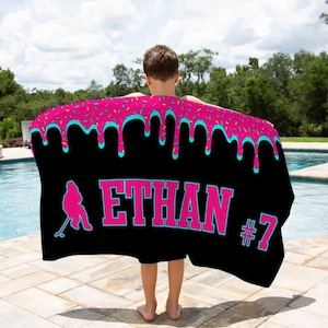 May include: A black beach towel with a pink and blue dripping icing design. The towel has the name "ETHAN" and the number "#7" printed on it.