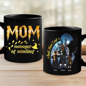 May include: Two black mugs with a Harry Potter theme. One mug has the text "MOM manager of mischief" in gold lettering with a wizard's hat and footprints. The other mug has the text "Best Mom Ever" with a silhouette of a family of three in front of Hogwarts.