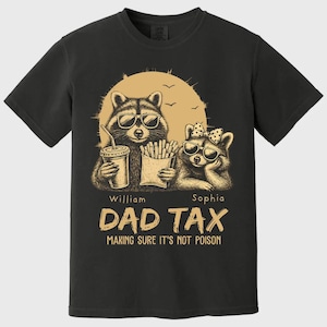 May include: Black t-shirt with a graphic of two raccoons in sunglasses, one with a drink and the other with fries. The text says "DAD TAX MAKING SURE IT'S NOT POISON" with the names "William" and "Sophia" below the raccoons.