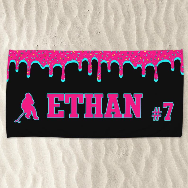 May include: Black beach towel with a pink and blue dripping icing design. The towel has a silhouette of a hockey player and the text "ETHAN #7".