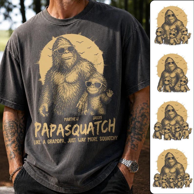 May include: Dark grey t-shirt with a Bigfoot graphic wearing sunglasses, and a smaller Bigfoot. The text reads "PAPASQUATCH" and "LIKE A GRANDPA, JUST WAY MORE SQUATCHY". The design is in shades of tan and brown.