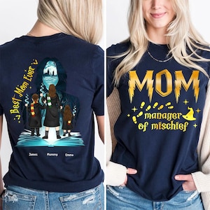 Peut inclure: Un t-shirt bleu marine avec un motif doré représentant le texte "MOM manager of mischief" avec un chapeau de sorcier et des empreintes de pas. Le dos du t-shirt présente un motif représentant une femme avec une cape sombre et trois enfants debout devant un livre. Le texte "Best Mom Ever" est sur le côté gauche du motif et les noms "James, Mommy, Emma" sont sous le motif.