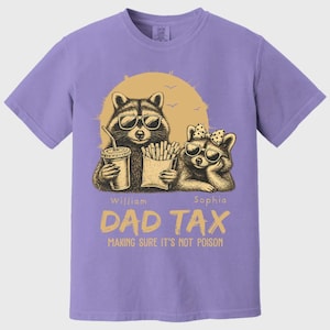 May include: A lilac t-shirt with a graphic of two raccoons wearing sunglasses, holding a drink and fries. The text "DAD TAX" and "MAKING SURE IT'S NOT POISON" are printed below the raccoons. The names "William" and "Sophia" are also printed.