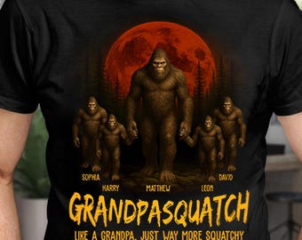 May include: Black t-shirt featuring a family of Bigfoot creatures in front of a red moon. The shirt reads "GRANDPASQUATCH" in yellow text, with the names of family members above the creatures. The phrase "LIKE A GRANDPA, JUST WAY MORE SQUATCHY" is below.