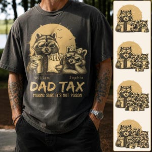 May include: Dark grey t-shirt with a raccoon family design. The graphic shows two raccoons wearing sunglasses, holding a drink and fries, with the text "DAD TAX" and "MAKING SURE IT'S NOT POISON".