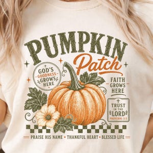 May include: A cream-coloured t-shirt featuring a graphic of an orange pumpkin with green leaves and flowers. The text reads PUMPKIN PATCH, GOD'S GOODNESS GROWS HERE, FAITH GROWS HERE, TRUST IN THE LORD PROVERBS 3:5, PRAISE HIS NAME, THANKFUL HEART, BLESSED LIFE.