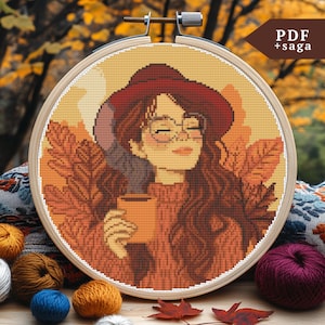 Könnte beinhalten: Kreuzstichmuster einer Frau mit langen braunen Haaren, die einen roten Hut und eine Brille trägt und eine Tasse Kaffee hält. Der Hintergrund ist in warmen Orange- und Brauntönen gehalten mit Herbstblättern.