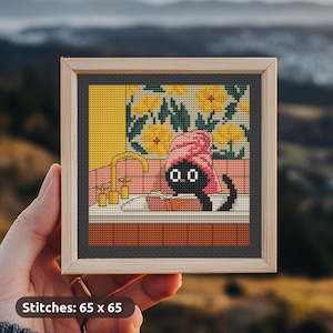Puede incluir: Arte de punto de cruz en un marco de madera que representa un gato negro con una toalla rosa en la cabeza, relajándose en una bañera. El fondo presenta flores amarillas y un grifo dorado. El texto "Stitches: 65 x 65" está en la parte inferior.