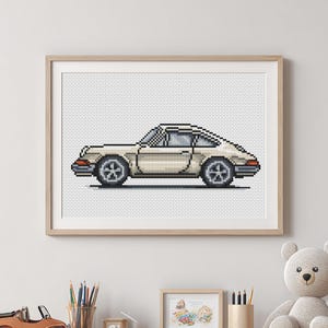 Könnte beinhalten: Gerahmter Pixel-Art-Druck eines cremefarbenen Sportwagens. Das Auto hat schwarze Räder und einen roten Akzent. Das Kunstwerk befindet sich in einem hellen Holzrahmen, ideal für die Dekoration eines Autoliebhabers.