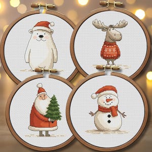 Op de afbeelding: Vier borduurringen met kruissteek met kerstthema's. Een ijsbeer, een eland, de kerstman en een sneeuwpop zijn afgebeeld, elk in feestelijke kleding. De ringen staan tegen een vage achtergrond met warme, gouden lichten.