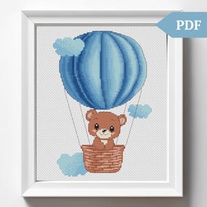Könnte beinhalten: Ein brauner Teddybär sitzt in einem Weidenkorb und fährt in einem blauen Heißluftballon mit weißen Wolken im Hintergrund.