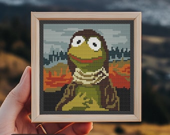 May include: Cross-stitch art of a cartoon character with large eyes, a green body, and a brown head, wearing a scarf. The artwork is framed in a light wood frame with a dark gray border. The background features a landscape with pumpkins. Text: Stitches: 65 x 65.