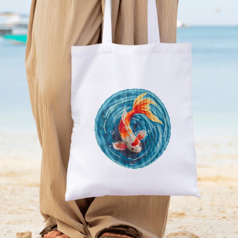 May include: White tote bag with a colorful fish design. The fish is orange, red, and white and is swimming in a blue circle with white swirls.