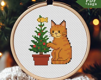 Könnte beinhalten: Kreuzstich-Stickerei in einem Holzrahmen mit einer rot getigerten Katze neben einem Weihnachtsbaum mit roten Ornamenten und einem Goldfisch. Der Text "PDF + saga" befindet sich in der oberen rechten Ecke. Der Hintergrund ist unscharf.
