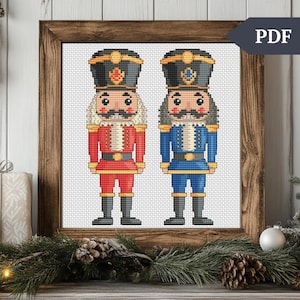 May include: Cross stitch pattern featuring two nutcracker soldiers. One is wearing a red uniform and the other is wearing a blue uniform. Both have black hats and white beards.