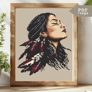 May include: Cross stitch pattern featuring a woman with long black hair and red and white feathers. The woman is looking up and has her eyes closed. The pattern is in a wooden frame.