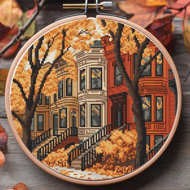 May include: A cross-stitch embroidery depicting a row of houses with a tree in front. The houses are painted in shades of red, white, and brown. The tree has yellow leaves and is set against a background of yellow leaves.