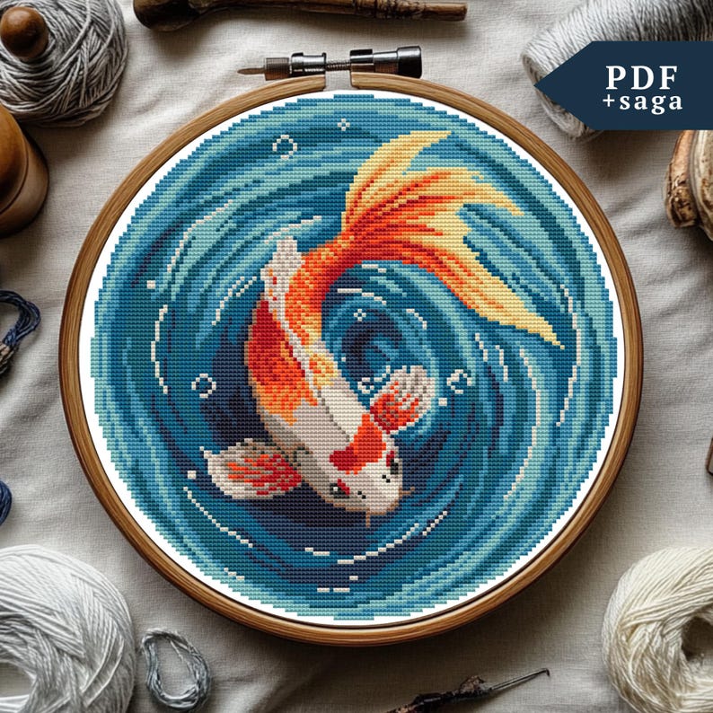 May include: A cross-stitch pattern of a goldfish swimming in a blue swirl. The goldfish is orange and white with a red fin. The pattern is in a round wooden embroidery hoop.
