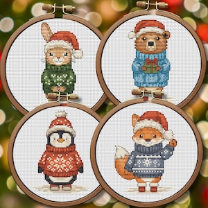 Op de afbeelding: Vier ronde houten borduurringen met kruissteekpatronen van een konijn in een groene trui, een beer in een blauwe trui met een cadeau, een pinguïn in een rode trui en een vos in een blauwe trui, allemaal met kerstmutsen op.