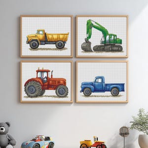 May include: Four framed cross-stitch artworks featuring construction vehicles. The collection includes a yellow dump truck, a green excavator, a red tractor, and a blue pickup truck. Each piece is set against a white grid background and framed in light brown.