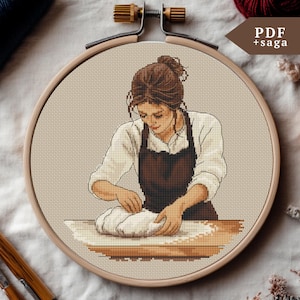 以下が含まれることがあります： 木製のフレームに入ったクロスステッチ刺繍。生地をこねる女性が描かれています。白いシャツと茶色のエプロンを着ています。「PDF + saga」の文字が右上。茶色、ベージュ、白の色使い。