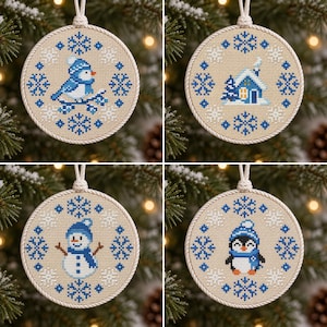 Può includere: Quattro ornamenti rotondi a punto croce su tessuto beige con motivi di fiocchi di neve blu e bianchi. I disegni includono un uccellino blu su un ramo, una piccola casa, un pupazzo di neve con sciarpa e un pinguino con cappello e sciarpa.