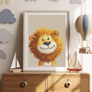 May include: A framed cross-stitch picture of a smiling lion with a golden mane and a beige background. The artwork is displayed on a wooden chest of drawers, with decorative sailboats and a hot air balloon nearby. The lion has a friendly expression.