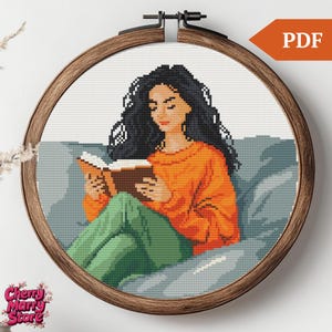 Puede incluir: Patrón de punto de cruz de una mujer con el pelo largo y negro sentada en un sofá y leyendo un libro. Lleva un jersey naranja brillante y pantalones verdes.