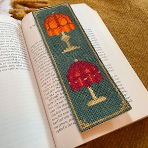 Close up angle of the stitched example of Fancy Lamps cross stitch bookmark pattern finished, resting inside a book on top of antique hard wood floors.