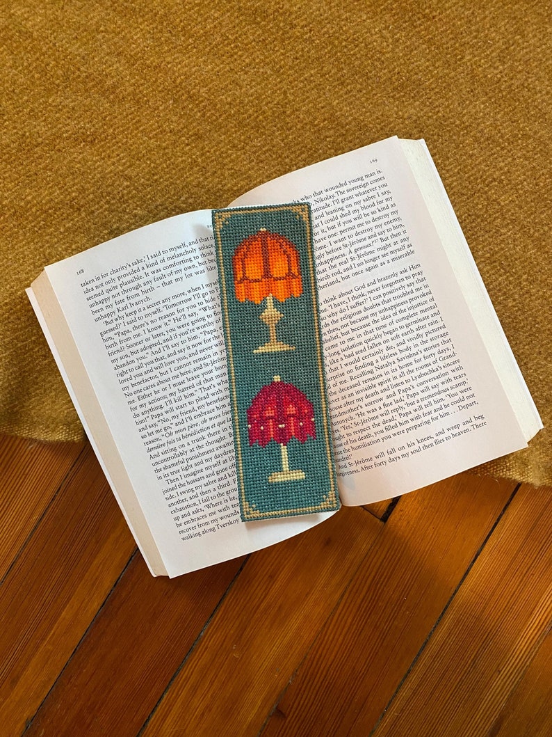 Stitched example of Fancy Lamps cross stitch bookmark pattern finished, resting inside a book on top of antique hard wood floors.