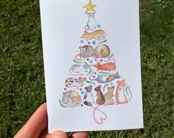 May include: A white greeting card featuring a watercolor illustration of a Christmas tree formed by a stack of various colored mice. The tree is topped with a yellow star and decorated with small colorful ornaments and green pine sprigs.
