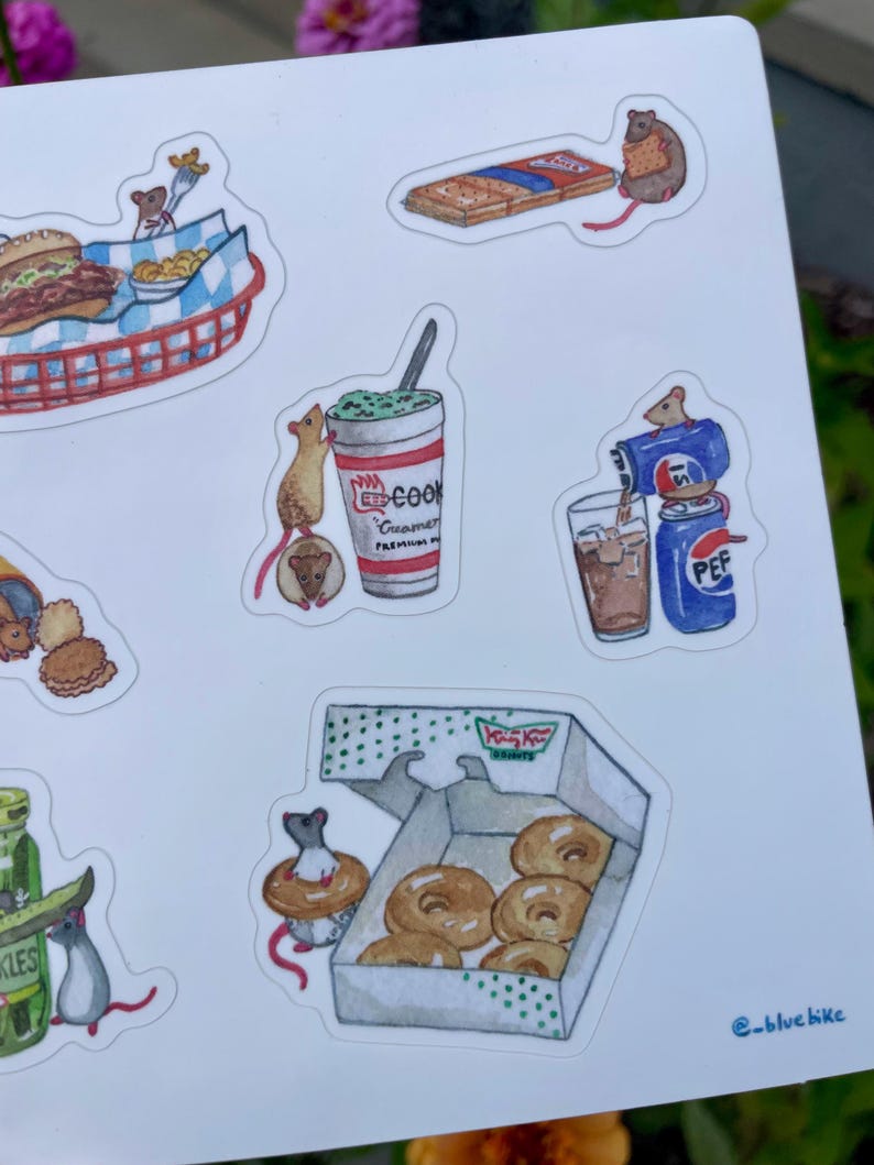May include: A sheet of watercolor stickers featuring mice interacting with various foods. The stickers include a burger and fries, a milkshake, a soda, a box of donuts, and a package of crackers. The stickers have a whimsical, cartoon style.