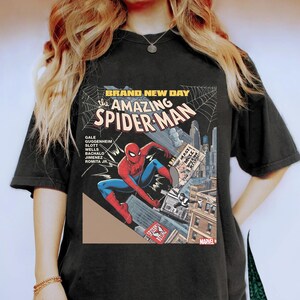 May include: Black t-shirt featuring a comic book cover design of Spider-Man. The graphic includes the text "BRAND NEW DAY" and "the AMAZING SPIDER-MAN". The superhero is depicted in a dynamic pose, with a cityscape backdrop and the Marvel logo.