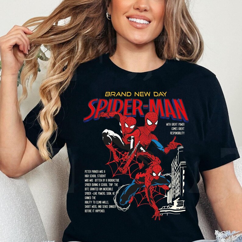 May include: Black t-shirt featuring a Spider-Man graphic. The design includes the words "BRAND NEW DAY" and "SPIDER-MAN" in red and white. The graphic depicts Spider-Man in action, with text describing his origin story.