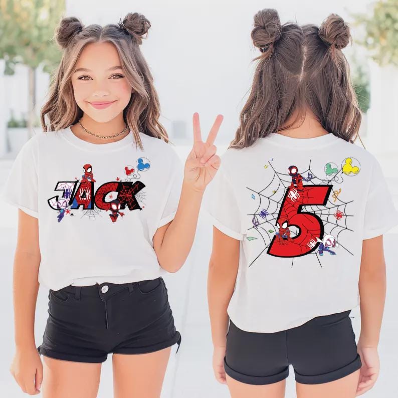 Pu&ograve; includere: T-shirt bianca con il nome "Jack" in stile fumetto, con grafica di Spider-Man. Il retro della maglietta mostra un grande numero rosso "5" con un disegno a ragnatela e personaggi di Spider-Man. La maglietta &egrave; indossata da una persona giovane.