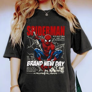Puede incluir: Camiseta negra con un dise&ntilde;o de Spider-Man agachado, con dise&ntilde;os de telara&ntilde;as y texto que dice "SPIDERMAN" y "BRAND NEW DAY". El dise&ntilde;o incluye la frase "WITH GREAT POWER COMES GREAT RESPONSIBILITY".