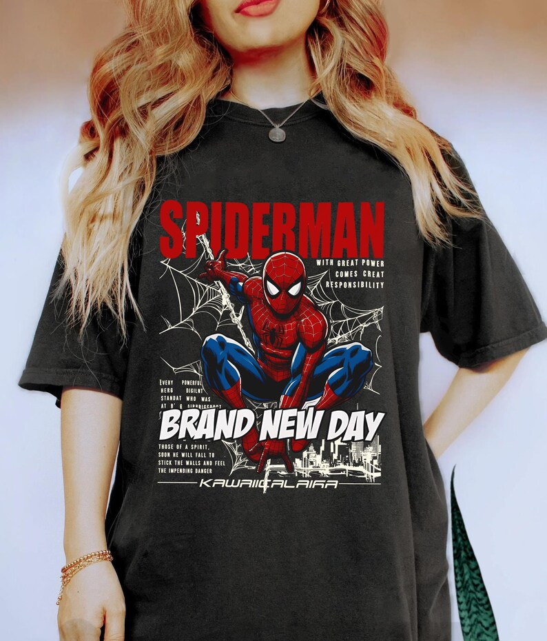 Puede incluir: Camiseta negra con un dise&ntilde;o de Spider-Man agachado, con dise&ntilde;os de telara&ntilde;as y texto que dice "SPIDERMAN" y "BRAND NEW DAY". El dise&ntilde;o incluye la frase "WITH GREAT POWER COMES GREAT RESPONSIBILITY".