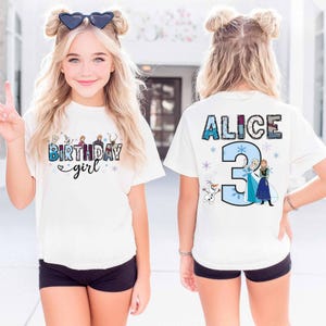 May include: A white short-sleeve t-shirt featuring a graphic print. The front displays the text "BIRTHDAY girl" with cartoon characters and snowflakes. The back shows the name "ALICE" above a large number "3" with cartoon characters and snowflakes.